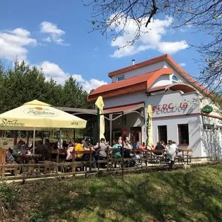 Terasa Bistra Pergola plná hostů, bílý domek s červenou střechou mezi borovicemi